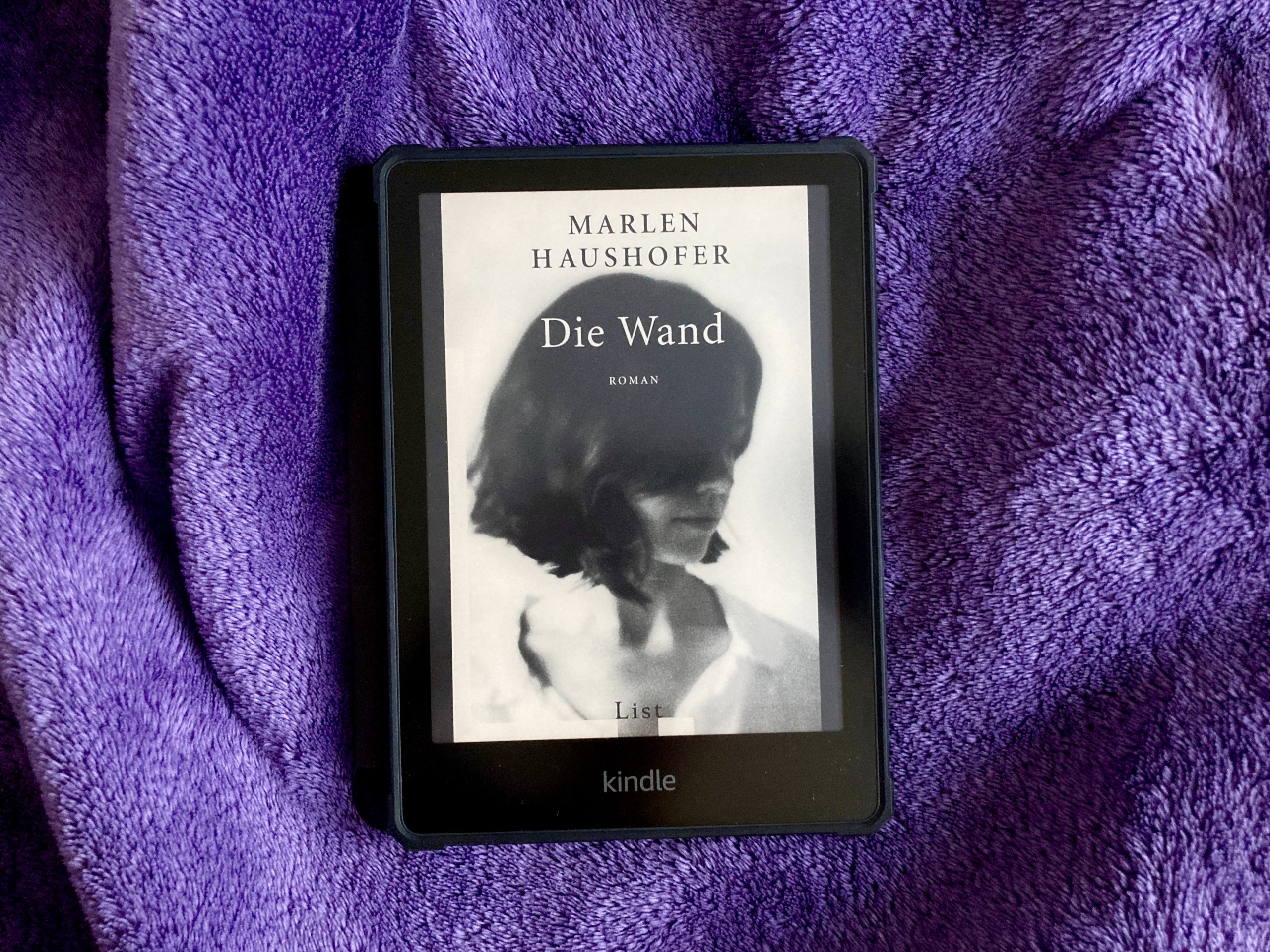 "Die Wand" von Marlen Haushofer auf einem Kindle E-Reader. Auf dem Cover ist das schwarz-weiße Foto einer Frau mit kinnlangen dunklen Haaren abgebildet, die sich so zur Seite dreht, dass ihre Haare den Großteil ihres Gesichts verdecken.
