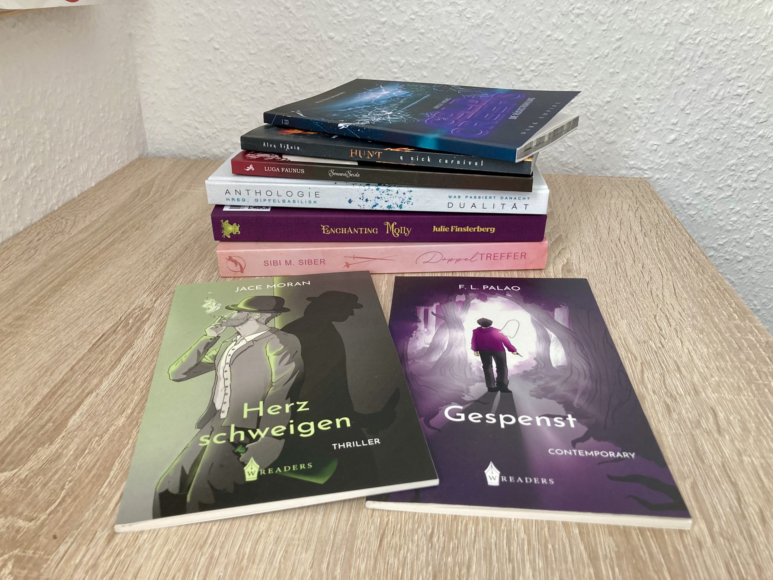 Ein Stapel mit folgenden Büchern: Doppeltreffer von Sibi M. Siber, Dualität – Anthologie herausgegeben von Gipfelbasilisk, Enchanting Molly von Julie Finsterberg, Cold Creeps – Die Rückstrahlung von Jules B. Asches, Hunt – A sick carnival von Alea Villain. Im Vordergrund liegen zwei sehr dünne Bücher: Herzschweigen von Jace Moran und Gespenst von F. L. Palao.
