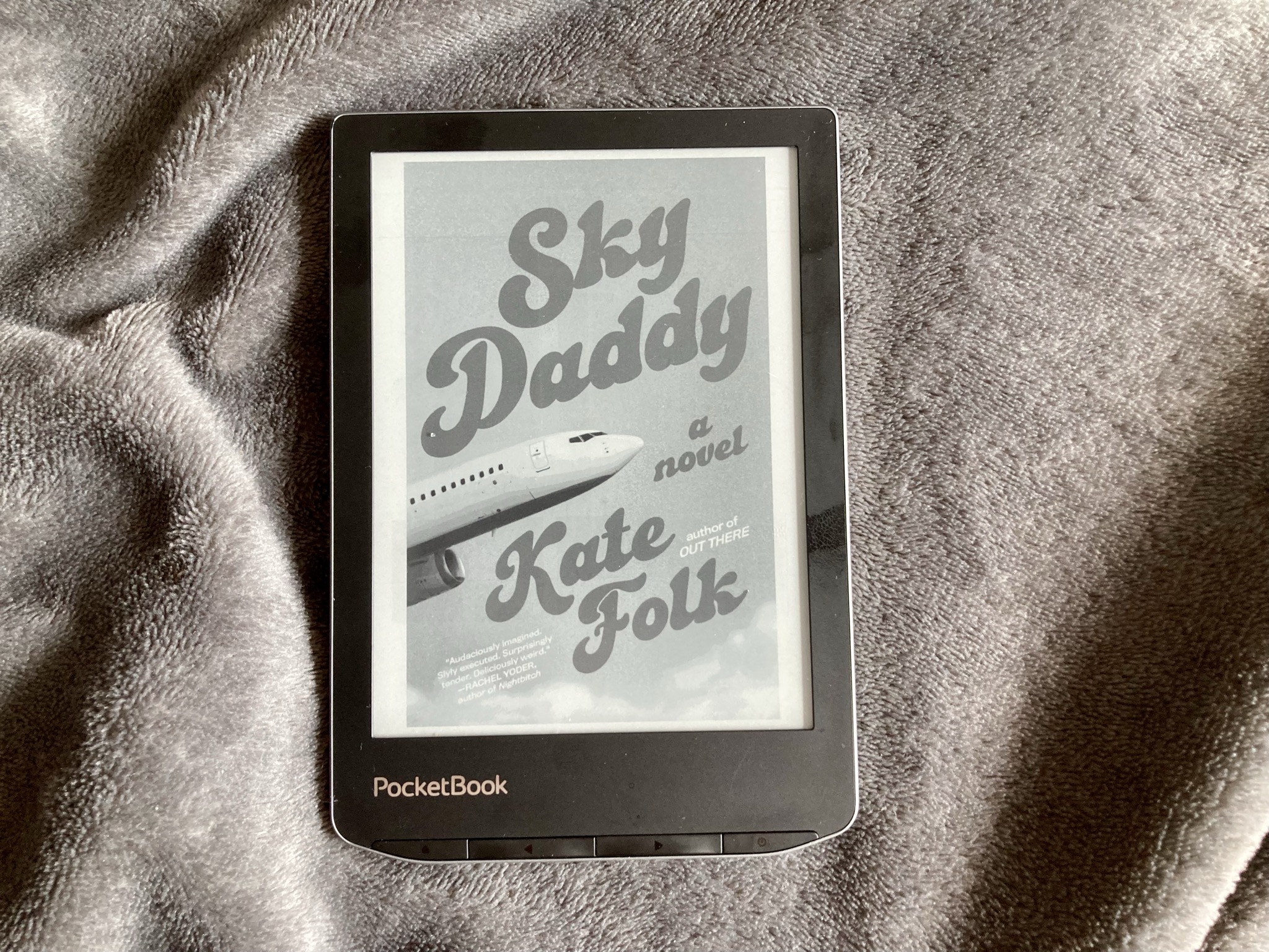 "Sky Daddy" von Kate Folk auf einem PocketBook E-Reader. Titel und Name der Autorin stehen in großer, funky Schrift vor einem Himmel, dazwischen schiebt sich ein Flugzeug nach oben.